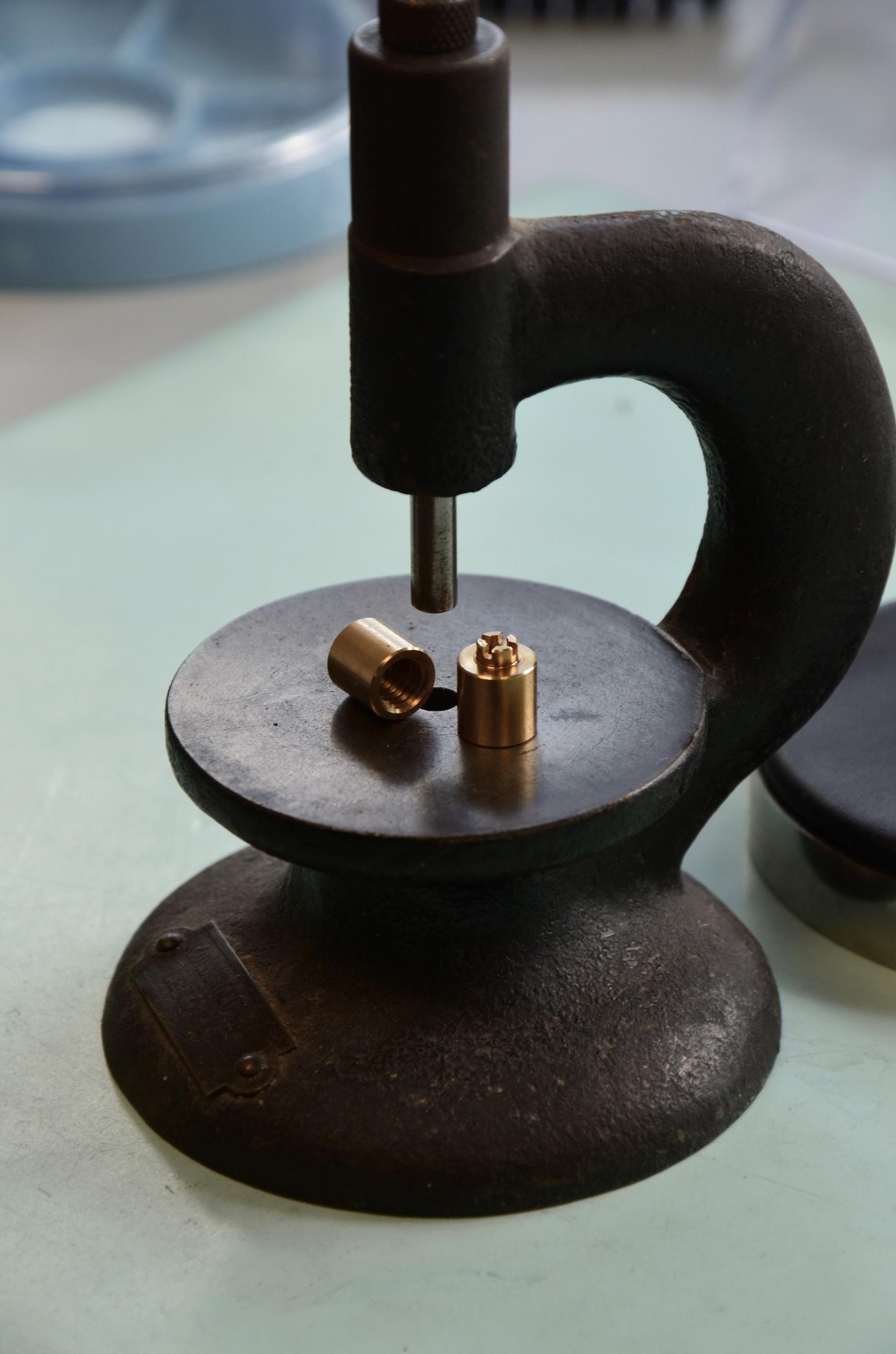 Presse manuelle et deux petites pièces cylindriques en laiton.